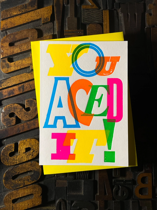 Colourful typographic letterpress card with bold overlapping neon letters spelling ‘You Aced It!’, perfect for celebrating exam success.
