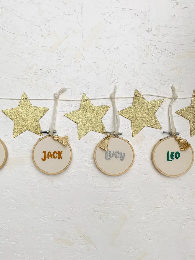 personalised name embroidered hoop bauble. set of 3 embroidered hoop baubles strung up on white wall.