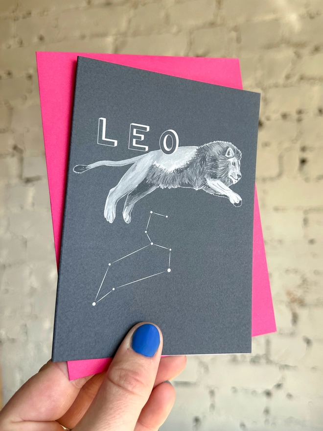 : a greetings card featuring a greyscale illustration of a zodiac style lion with the text “LEO” with a neon pink envelope