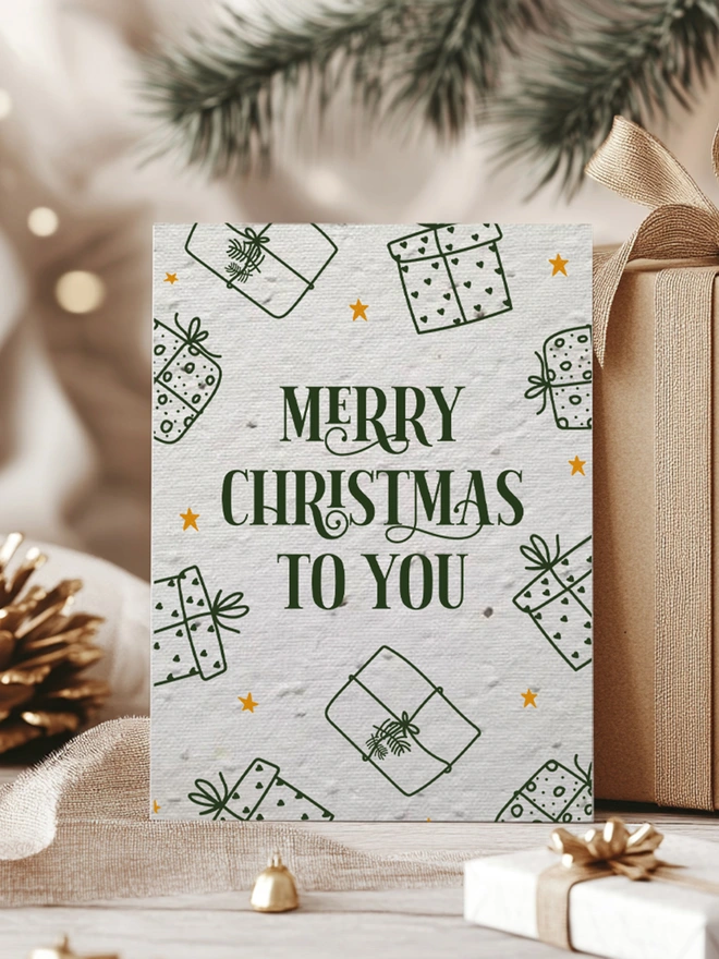 Christmas Card with 'Merry Christmas To You' with presents around the edge of the card. The card is surrounded by presents with gold ribbon