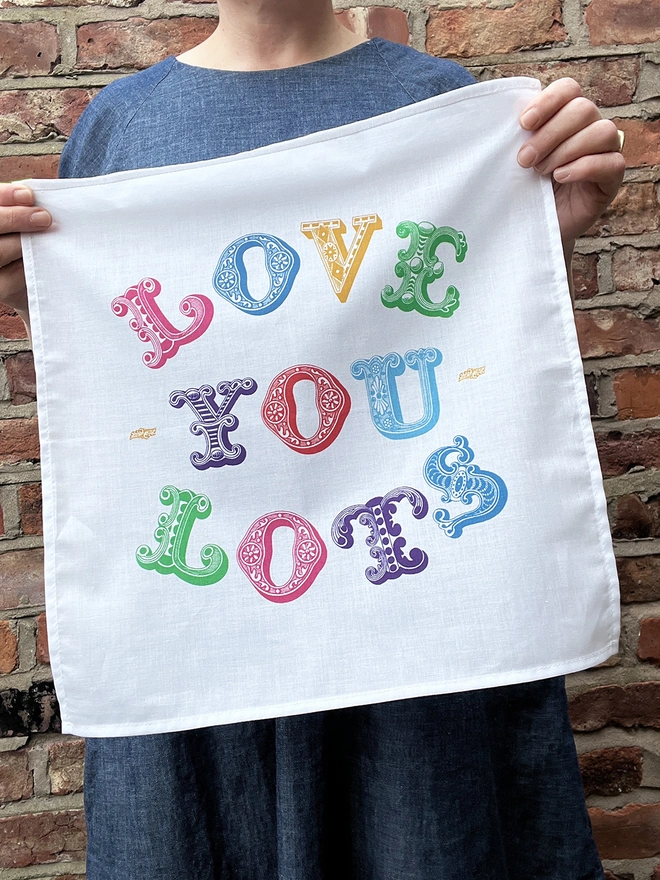 A Mr.PS Love You Lots Multicoloured Printed Handkerchief held by a white woman wearing a denim dress in front of a brick wall