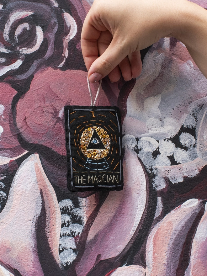 A handcrafted felt ornament with sequins and embroidery depicting "The Magician" tarot card. Colourful embroidery with an eye inside a crystal ball. 