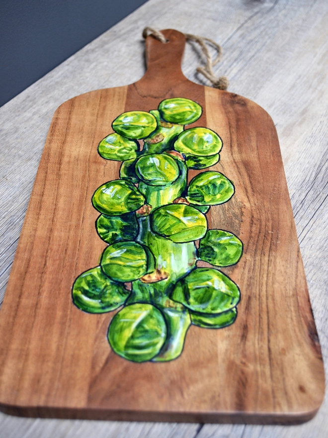 A wooden serving board with a handpainted design of Brussels sprouts