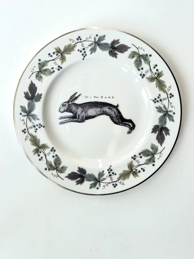 a vintage plate with decorative ornate border of grey blue leaves, in the centre i have printed a vintage black and white illustration of a hare
