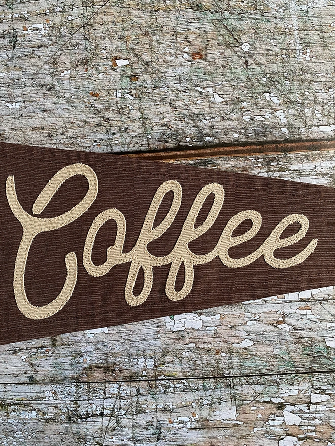 Detail of an espresso brown 'Send Coffee' pennant flag showing the word Coffee in a latte coloured canvas