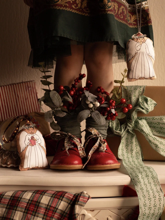 2 christmas tree angel decorations next to a little girl with Christmas tree foliage in her socks vintage vibe