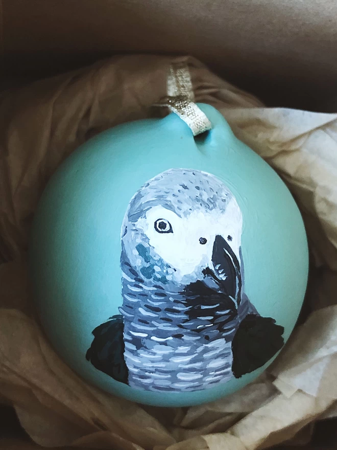 An illustration of a grey parrot on a mint green Christmas bauble