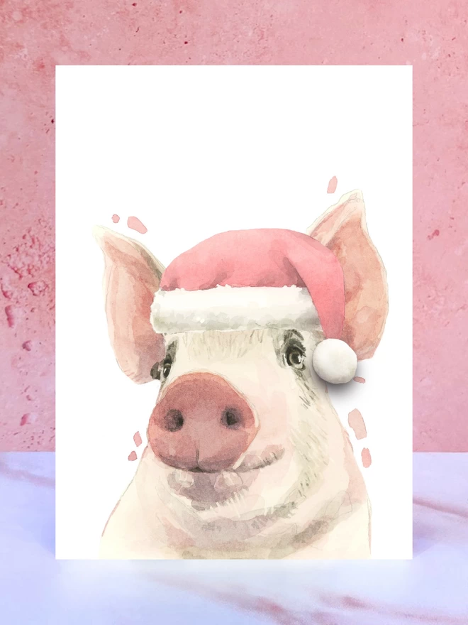 A Christmas card featuring a hand painted design of a pig, stood upright on a marble surface. 