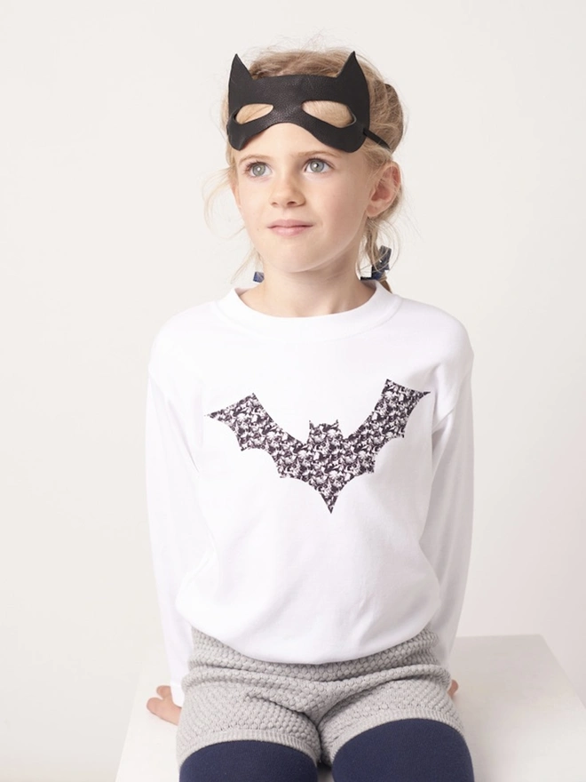 A 5 year old girl wearing a white cotton t-shirt with a monochrome Liberty fabric bat sewn on the front. 