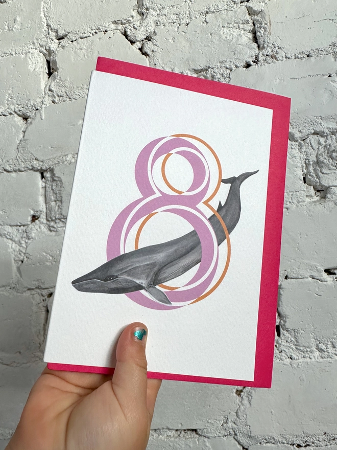white card with a big pink number 8 and an illustration of a fin whale with a neon pink envelope