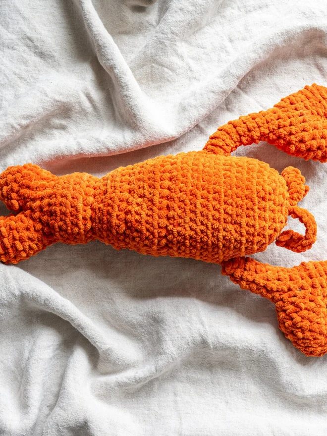 Chunky Chenille Cuddly Crochet Crustacean Lobster Plush, an orange lobster plush sitting on a white table cloth. 