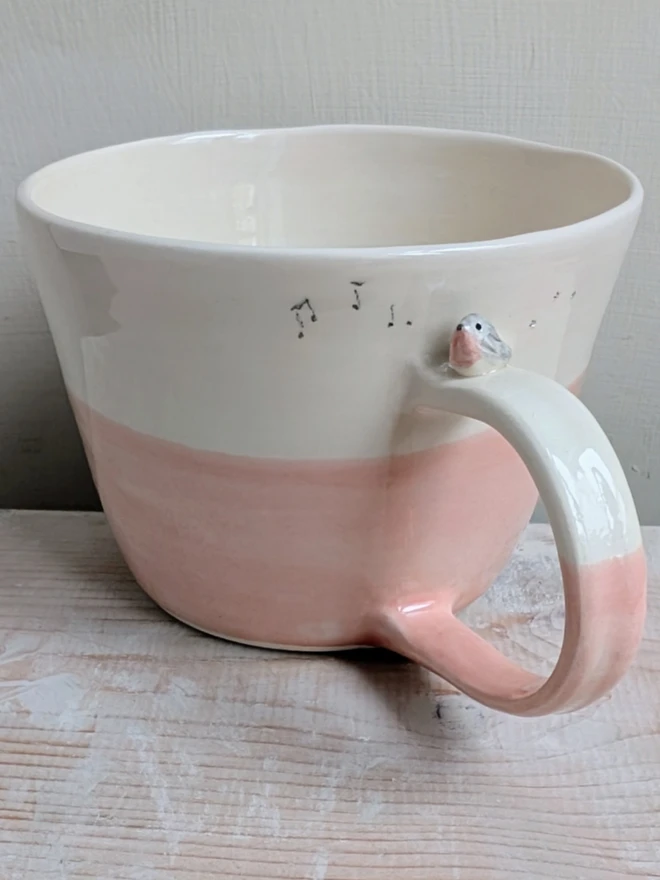 ceramic pink bird cup with a tiny pink and grey robin bird on the handle and musical notes and bird prints on the mug
