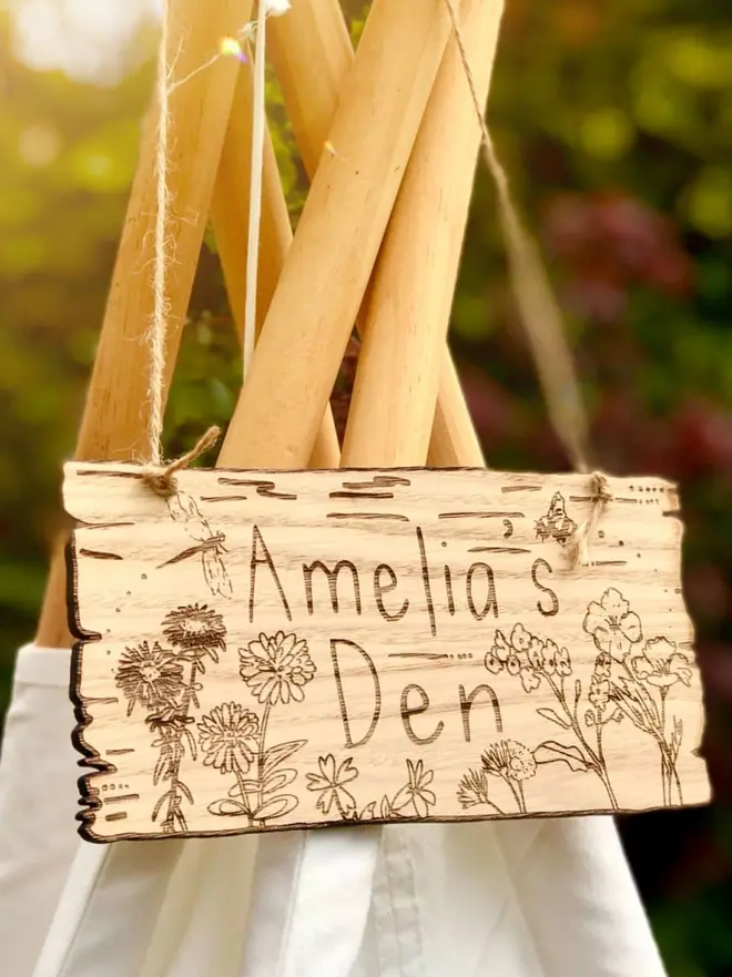 Wild Flowers Den Sign, a wooden sign hanging from a play teepee that reads "Amelia's Den" surrounded by engraved wild flowers.