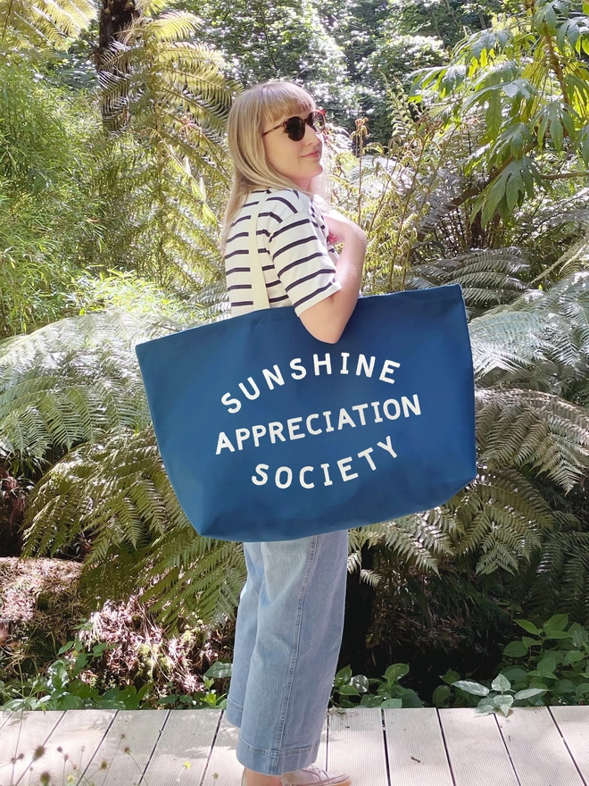 Model holding an blue oversized tote bag with Sunshine Appreciation Society slogan