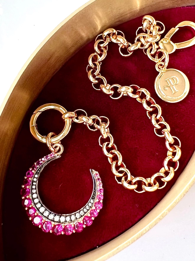 Pink crescent moon stone set charm on a gold belcher chain bracelet inside red velvet jewellery box