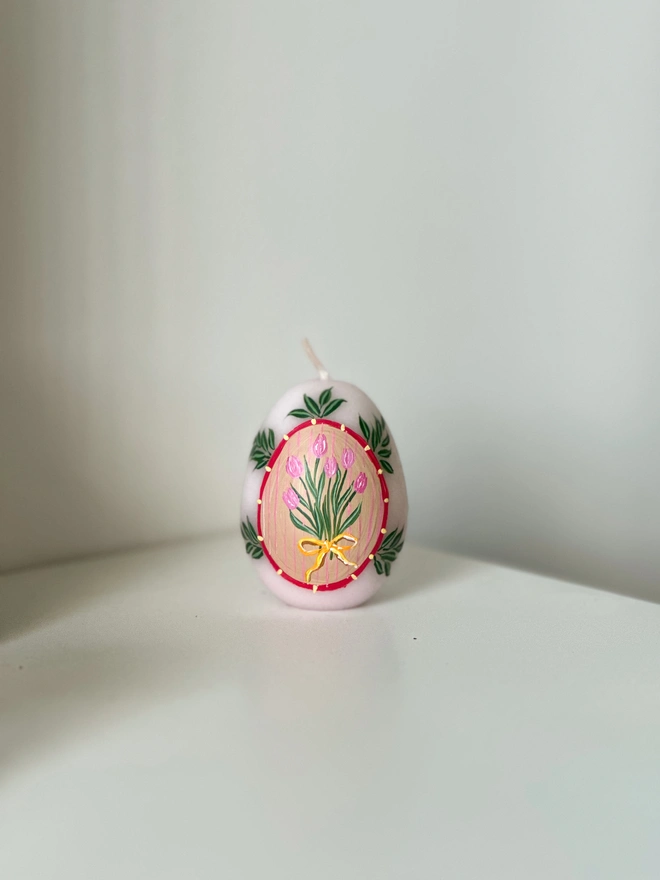 Hand Painted Easter Egg Candle Pink Tulips, an Easter egg candle sitting on a plain surface. It's Easter and floral design wraps around it. 