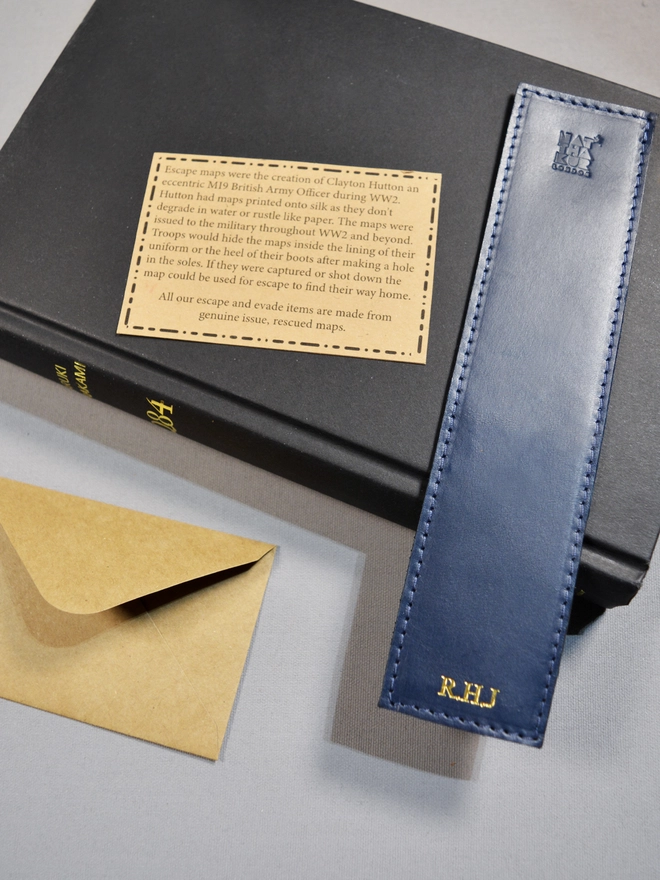 A navy blue ethically produced vegetable tanned Italian leather bookmark lined with an original silk escape map from the Cold War personalised with silver foil initials with the initials R and H and J by natthakur