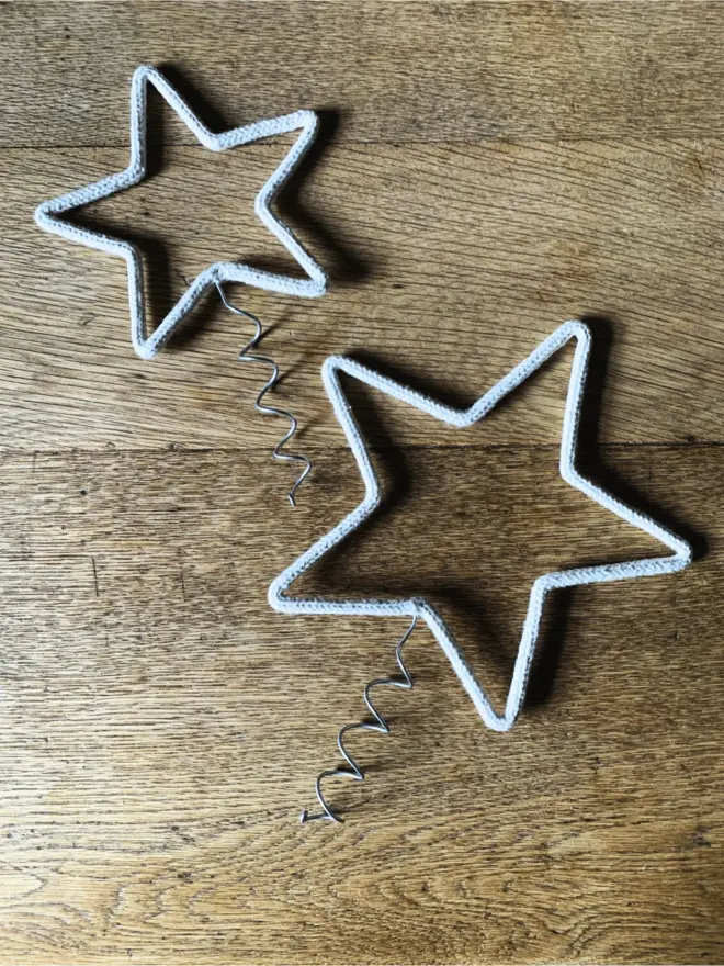 Two string wrapped wire star tree toppers with close up of the small and large coils on an oak table