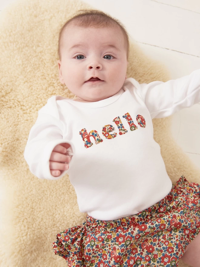 hello appliquéd in Liberty print floral print on a white cotton bodysuit worn by a happy baby
