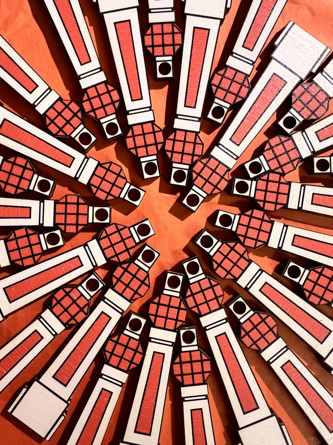 Small white and orange wooden tree decoration in the shape of Margate Lido sign. There are lots of them arranged in a circular patten in a flat lay on an orange card background.