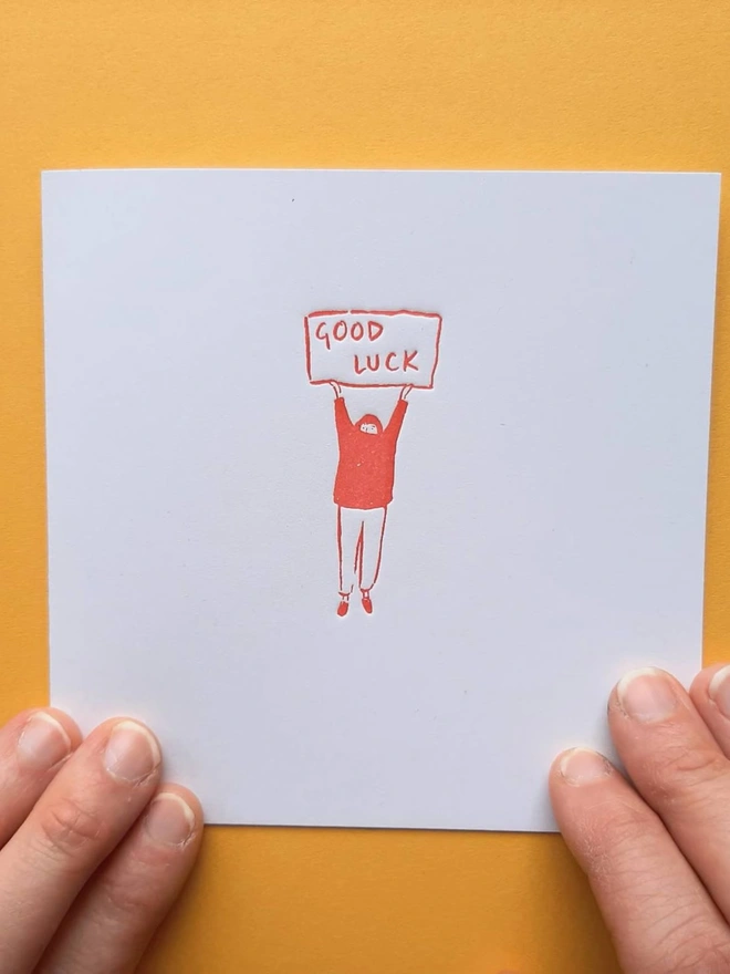 'Good Luck' Letterpress Handprinted Greetings Card, person holding white good luck card with an orange design against a yellow background. 