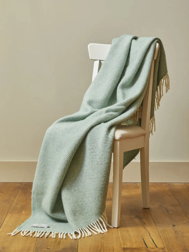 Lambswool egg shell throw with white tassels draped over a wooden chair. 
