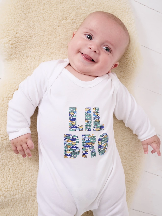 Lil Bro appliquéd on a white cotton baby romper in a vintage cars and busses Liberty print. worn by a happy baby