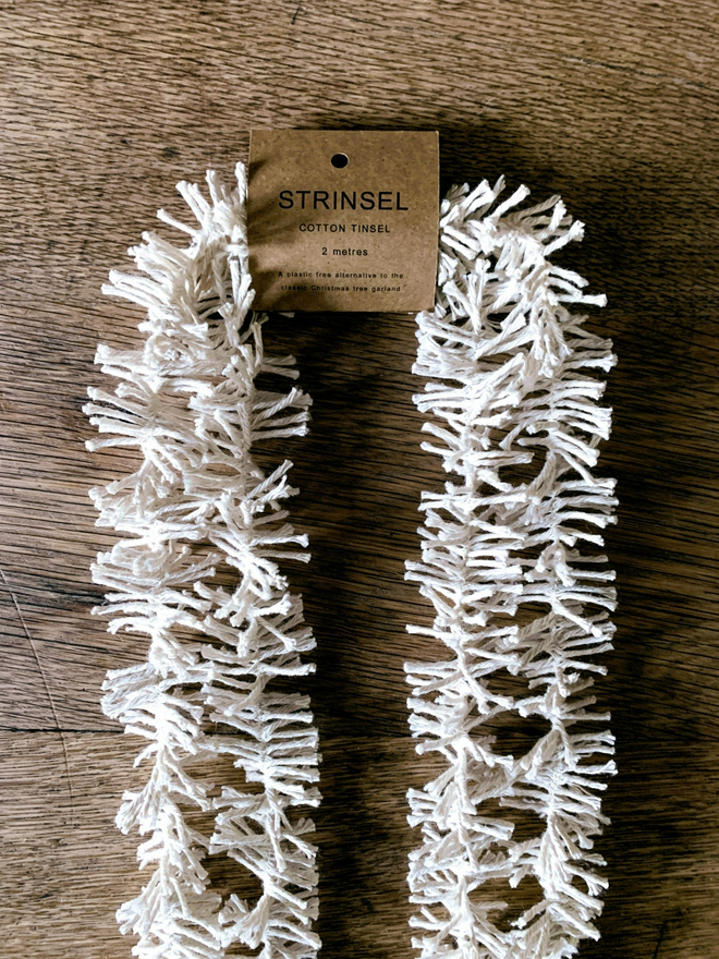 2 metre length of white Cotton Strinsel (plastic free string tinsel) showing label on oak background