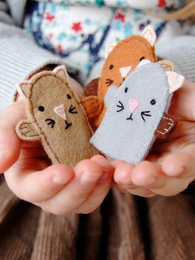A young child holds three homemade felt kitten finger puppets in her hands.