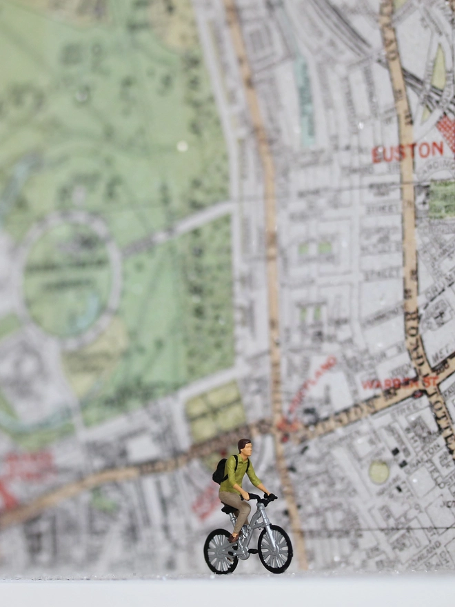 Artbox comprising a tiny man on a bike cycling against sparkling map backdrop 