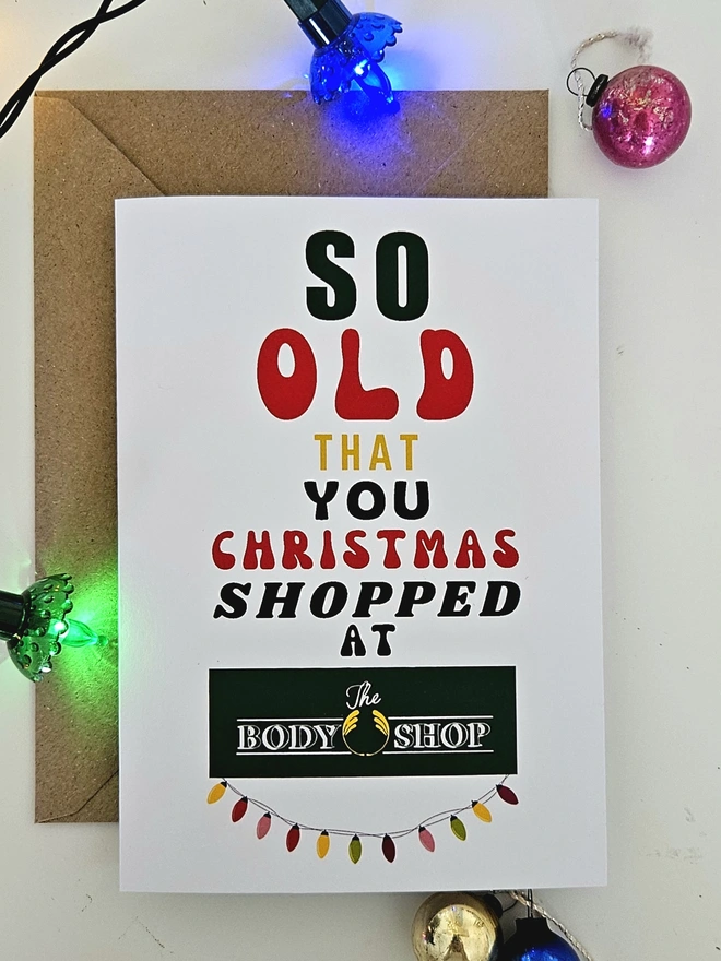 A photograph of the front of a humorous A6 greeting card illustrated using brightly coloured text and the retro shop logo. The text says so old that you Christmas shopped at The Body Shop with a string of colourful fairy lights.
