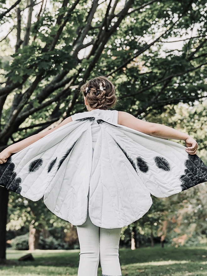 a child wearing a Cabbage White Butterfly costume with their arms and wings outstretched