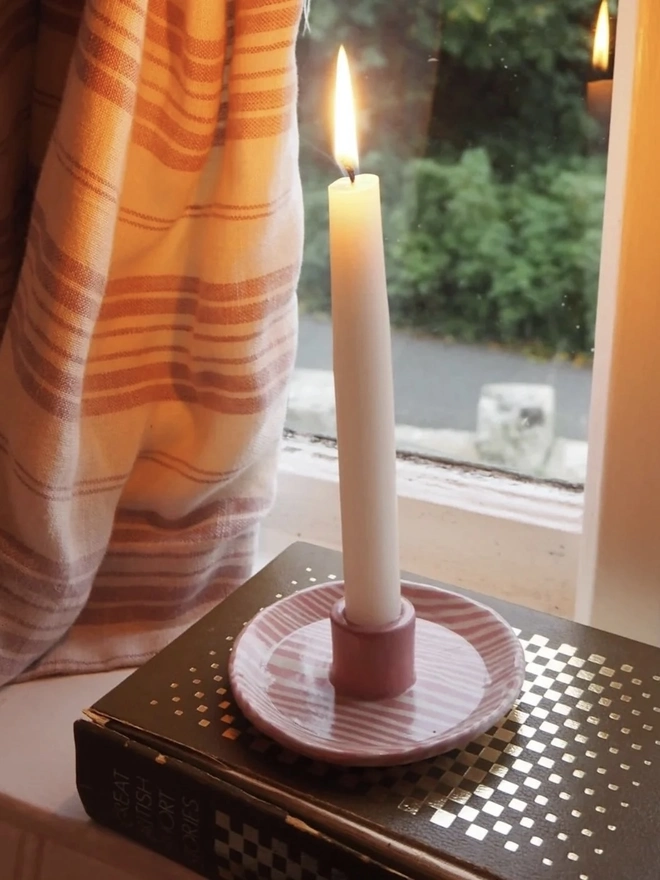 Ceramic Patterned Candlestick Holder, a colourful candlestick holder sitting on a window sill. It is accompanied by a lit candle. 