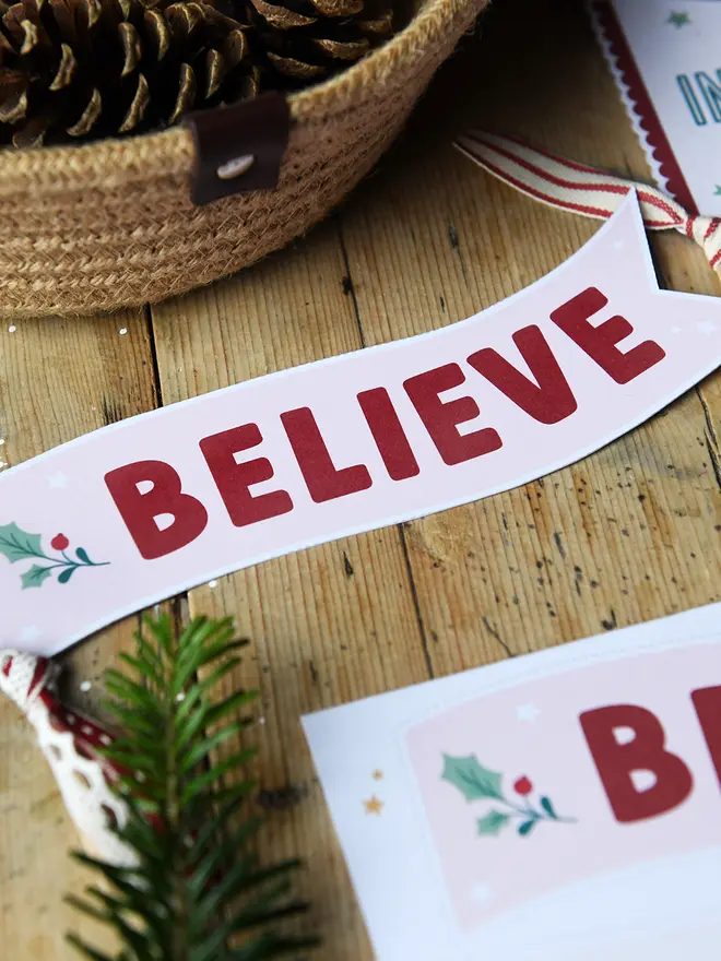 A cut out cardboard Christmas Believe flag lays on a wooden table