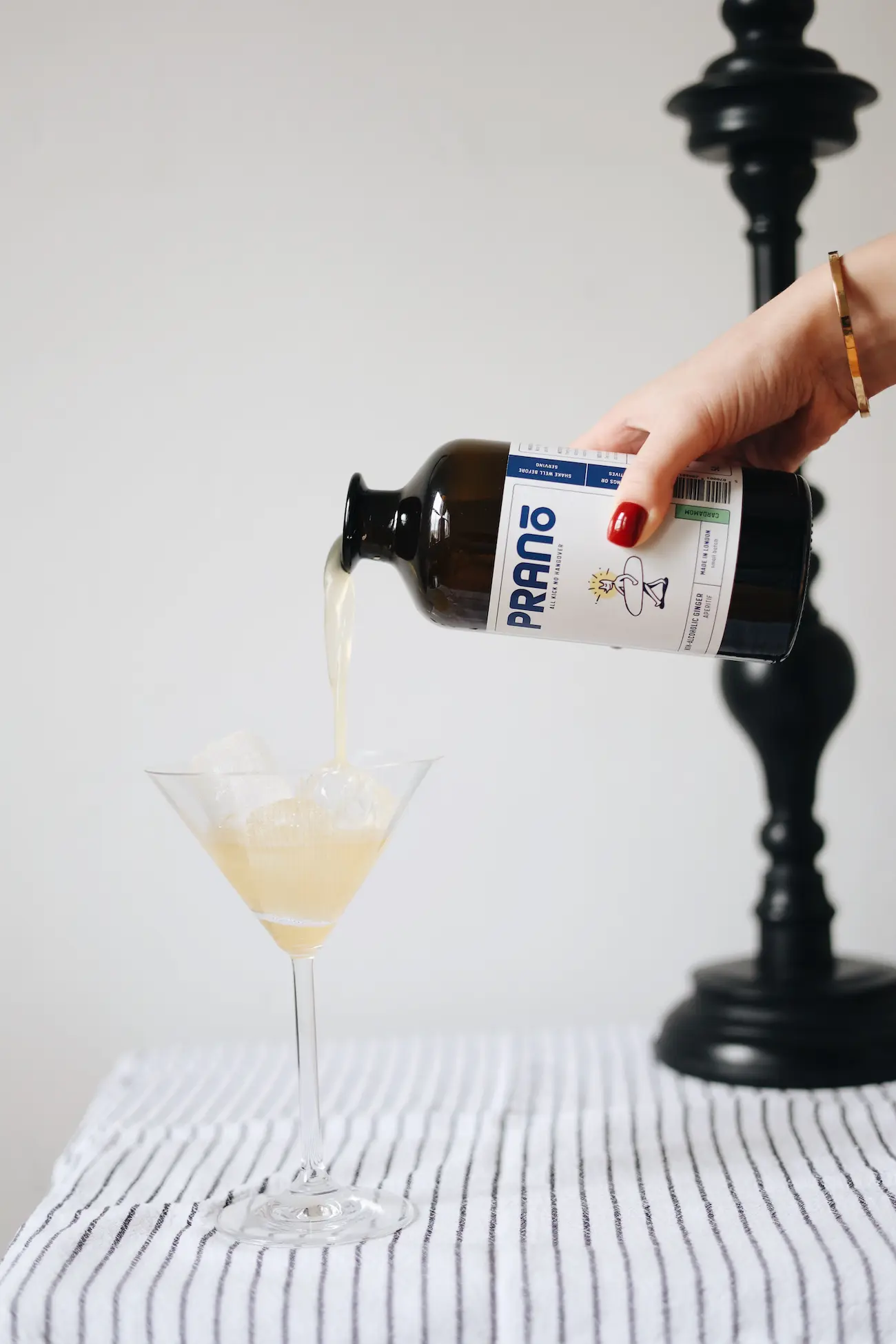 Hand pouring a bottle of prano into a martini glass, sitting atop a striped tablecloth