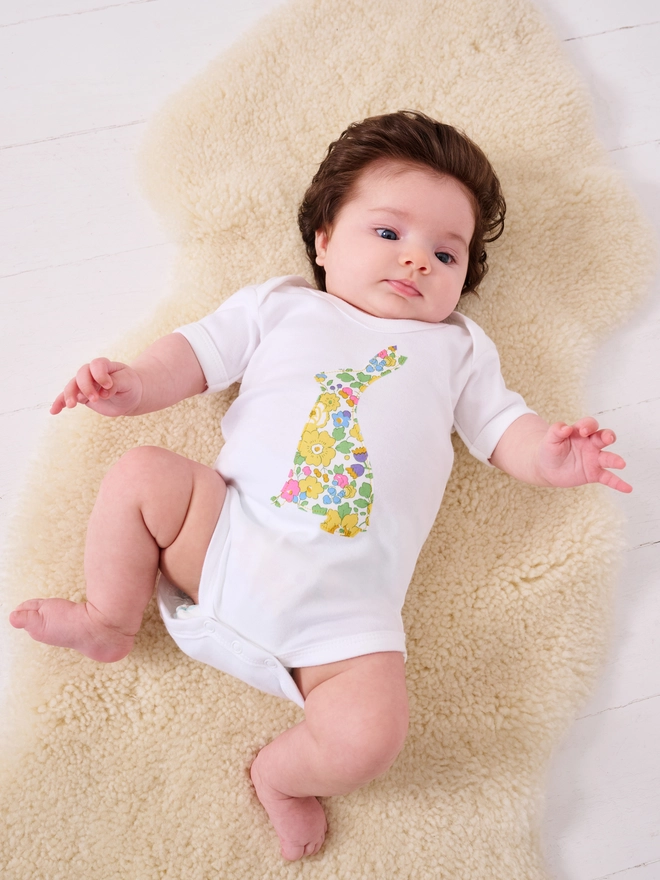 a baby wearing a cotton baby bodysuit babygrow with an easter bunny cut from yellow floral liberty print on the front 