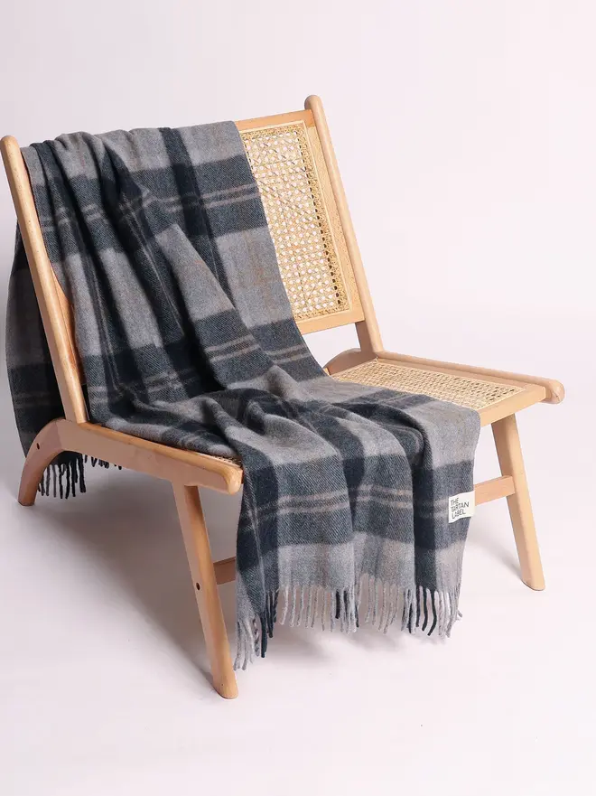 Bannockbane Silver, a grey blanket draped over a wooden chair on a white surface against a plain backdrop. 
