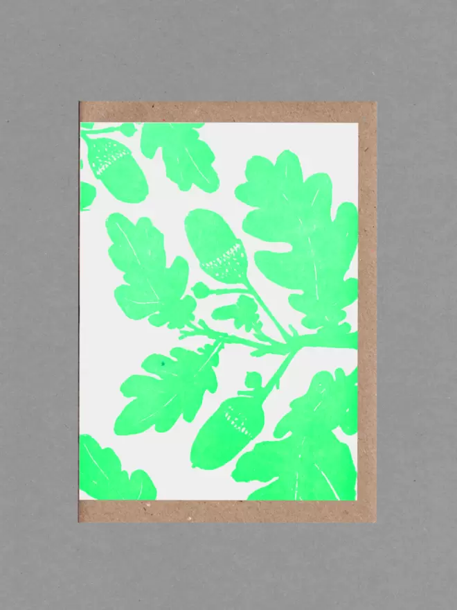 Greetings card with an illustration of oak leaves and acorns in bright green. Behind the card is a brown envelope on a grey backround.