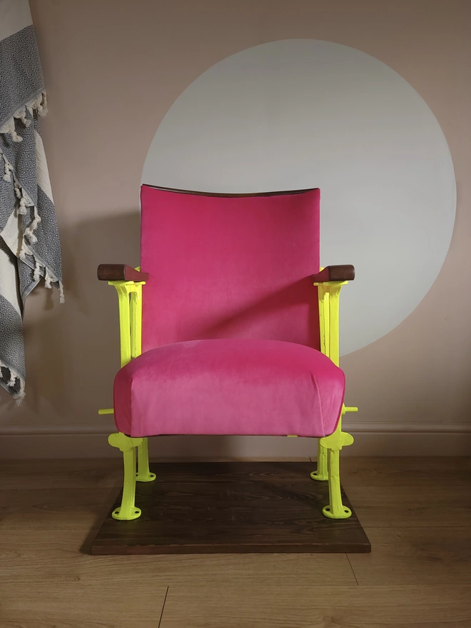 Front view of hot pink vintage cinema seat with neon yellow legs, seat down