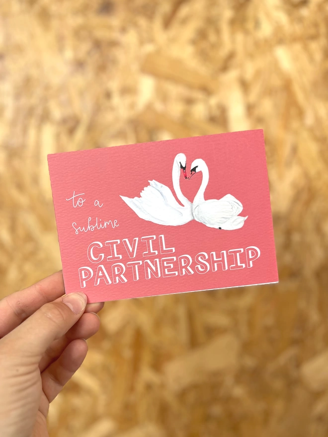 a greetings card with a deep pink background featuring two swans with their necks meeting in a heart shape, and the phrase “to a sublime CIVIL PARTNERSHIP”