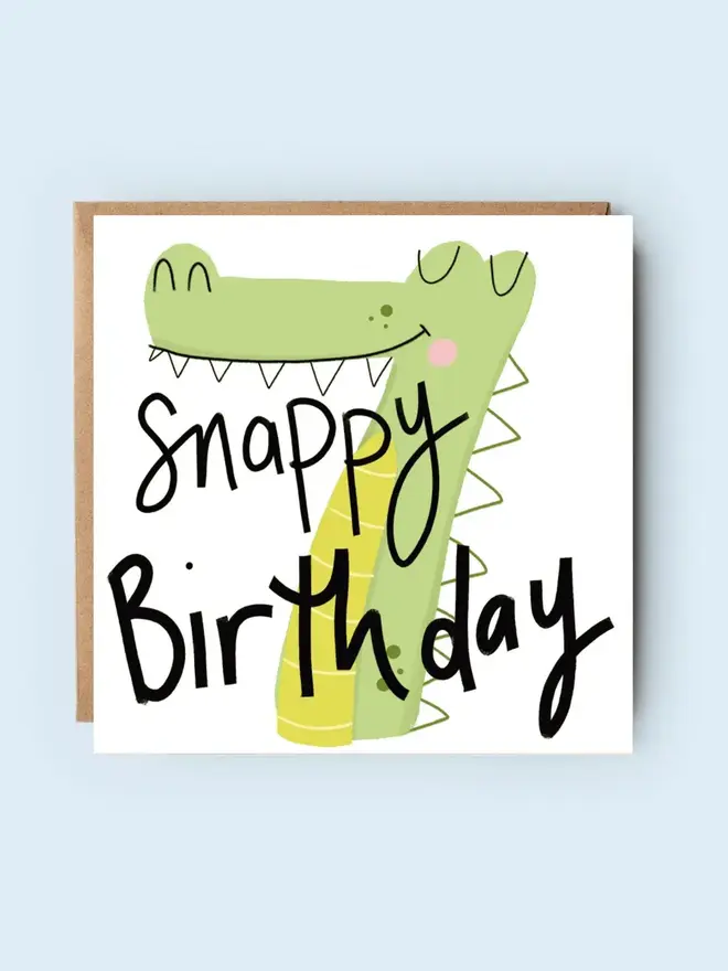 'snappy' illustrated 7th birthday card. card featuring green crocodile shaped like a number 7.