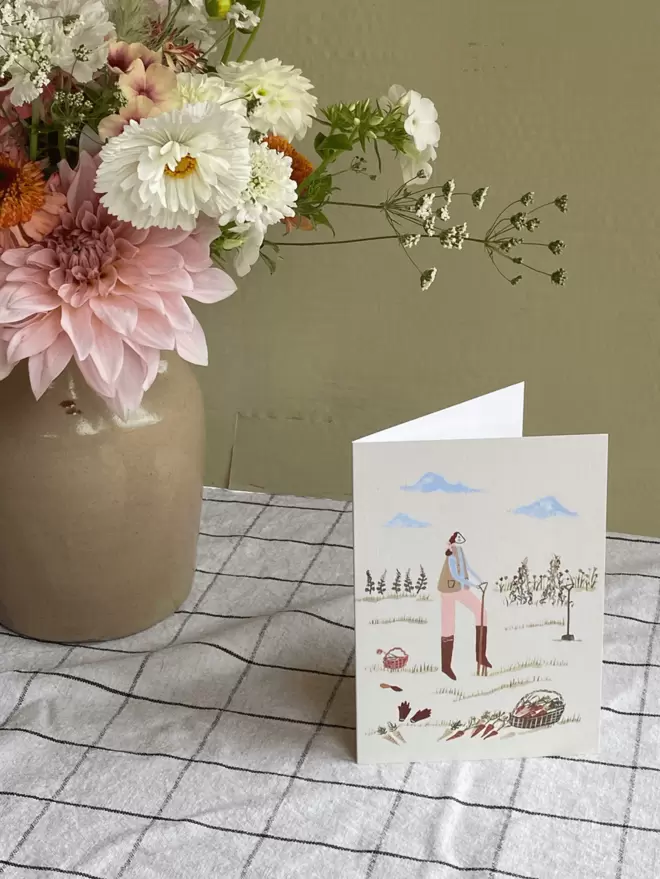 pink flowers on a gingham table cloth next to greetings card.