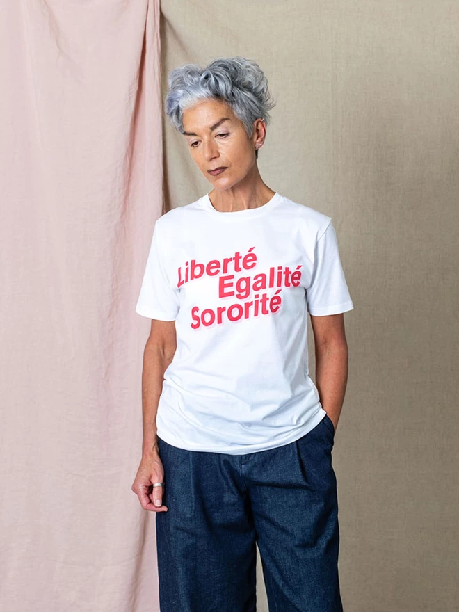 Model wearing a white organic cotton t-shirt with the words  LIBERTÉ, EGALITÉ, SORORITÉ written in red with a pink boarder