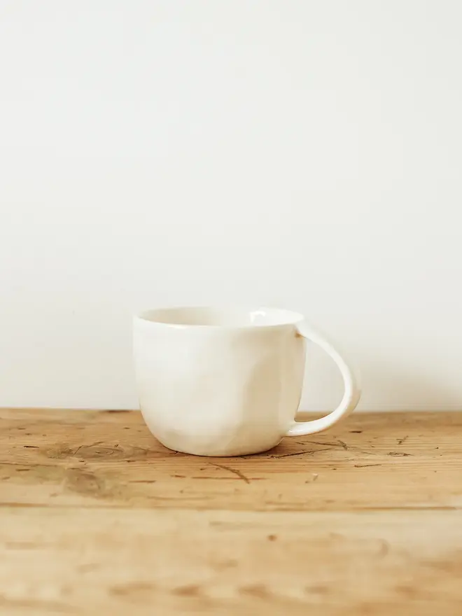 handcrafted stoneware mug. a white stoneware mug on a wooden bench.