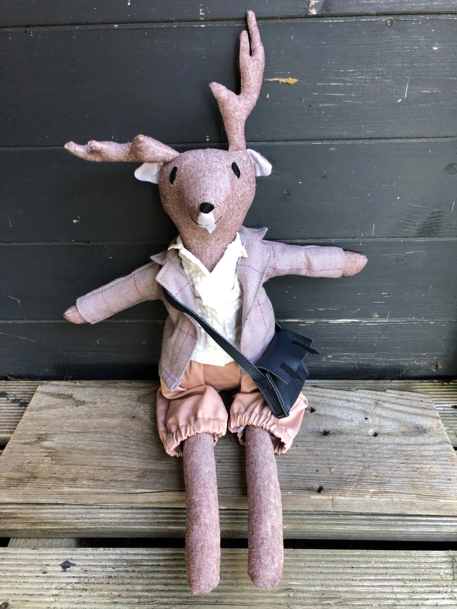 Soft toy reindeer,wearing lilac tweed jacket,white shirt, pink shorts and blue leather satchel