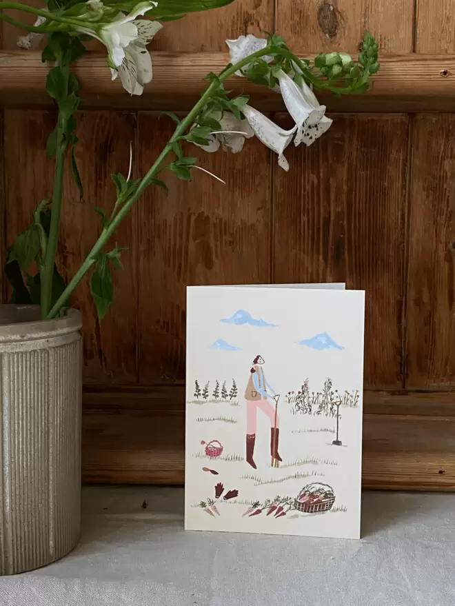 Foxgloves in a vase next to greetings card with girl on doing gardening