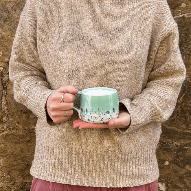 Shoreline Large Round Mug, a woman wearing a jumper holding a colourful mug in her hands in front of her. 