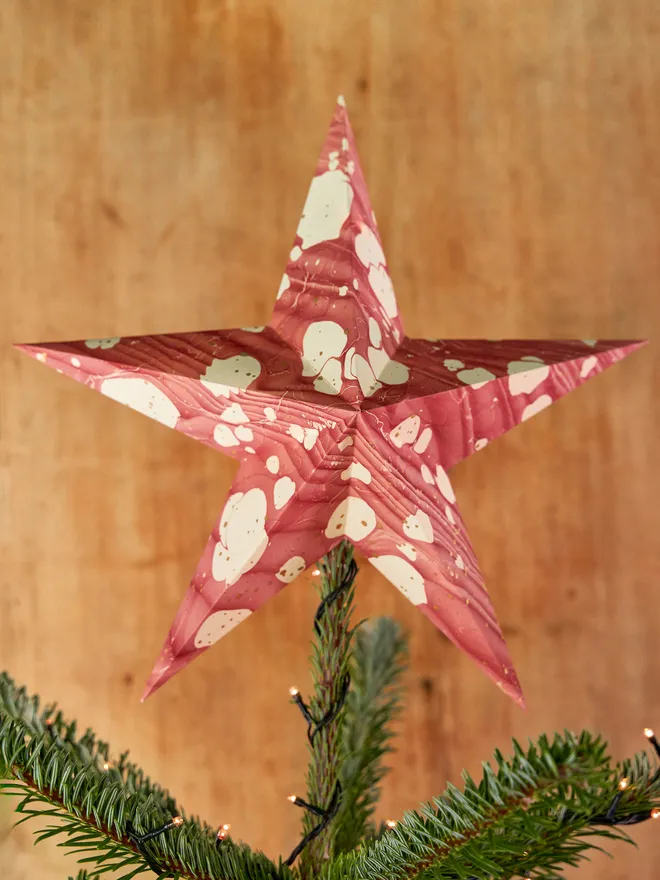 Red toned marbled paper star tree topper, on top of a Christmas tree against a wooden background