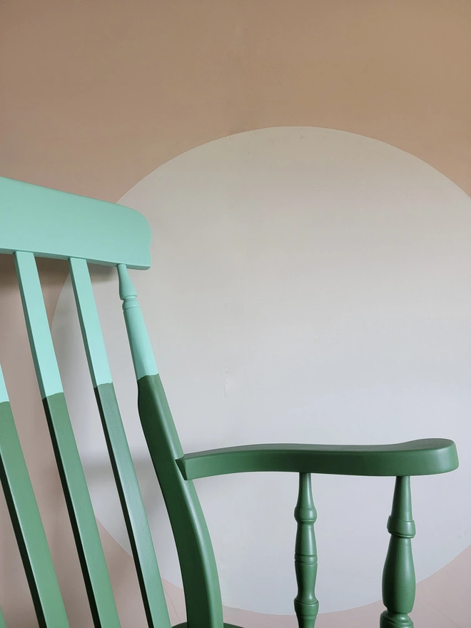 Corner view of rocking chair painted green and mint with pink background
