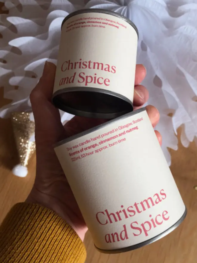 Christmas and Spice Wax Candle - a pale pink and red tin in a small and big size held up against some christmas items 